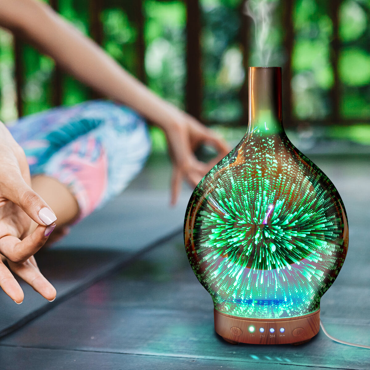 A person meditates cross-legged beside the glowing Rio ELLA Aroma Diffuser, Humidifier, and Night-Light, which emits soothing vapor and colorful light for a relaxing outdoor ambiance.
