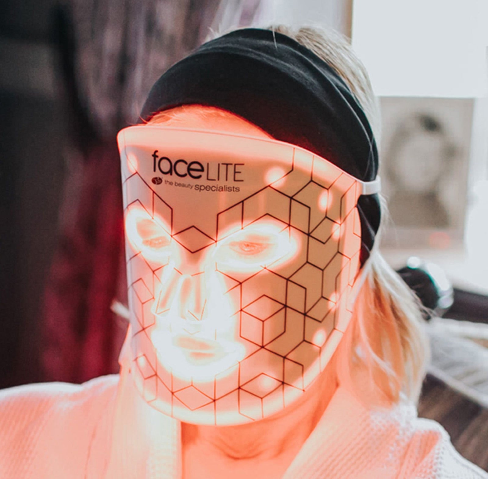 blonde lady relaxing wearing facelite beauty boosting LED face mask with red and infrared lights illuminated