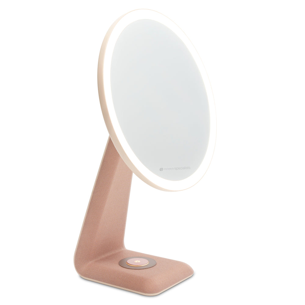 The Rio TrueColour High Performance Makeup Mirror features a round, high-clarity design with a soft white LED ring, set on a pink fabric-textured stand. A touch button at the base and angled frame reflect refined simplicity.
