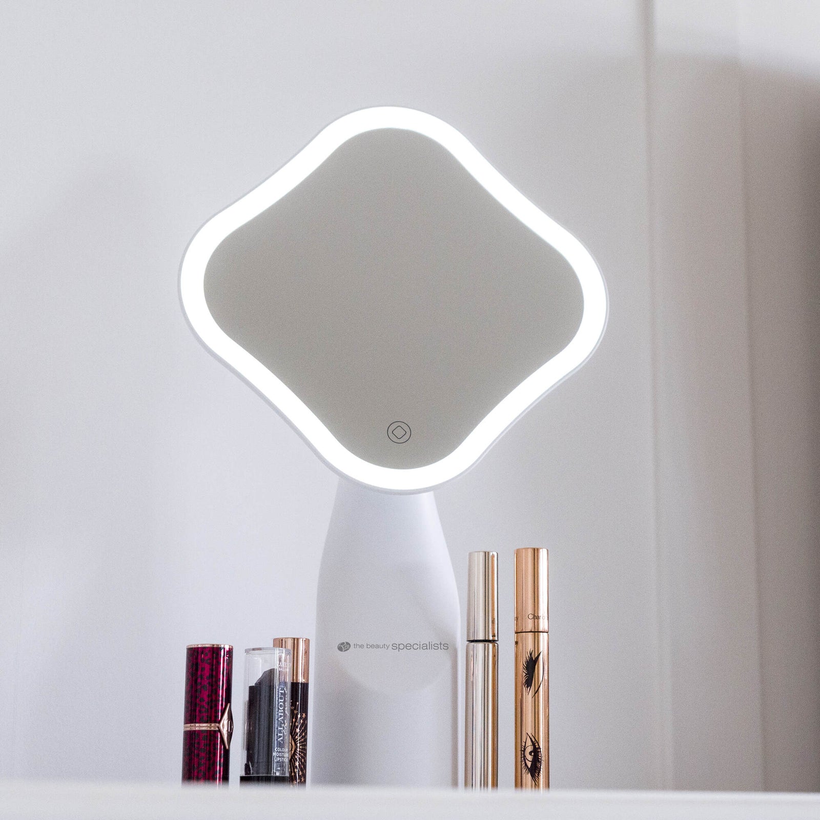 The Rio Illuminated Full Size Beauty Mirror with an LED border and rounded square design sits on a white surface, accompanied by two mascara tubes and two lipsticks placed in front of the vanity mirror.