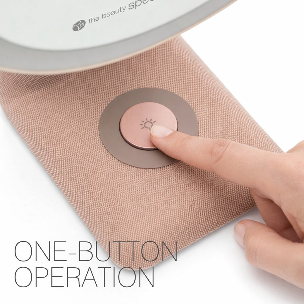 A hand presses a circular button with a light icon on the textured, pinkish base of the Rio TrueColour High Performance Makeup Mirror. Text on the image reads ONE-BUTTON OPERATION, highlighting its refined simplicity.