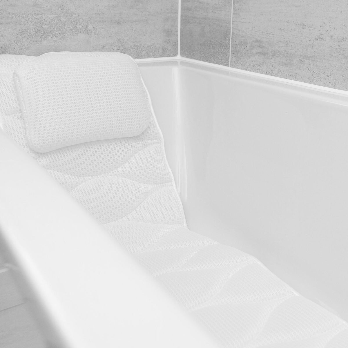 The Rio Luxury Bath Mat & Pillow in white create a clean, modern look in the tub, perfectly complementing light-colored tiled walls for ultimate bathing indulgence.