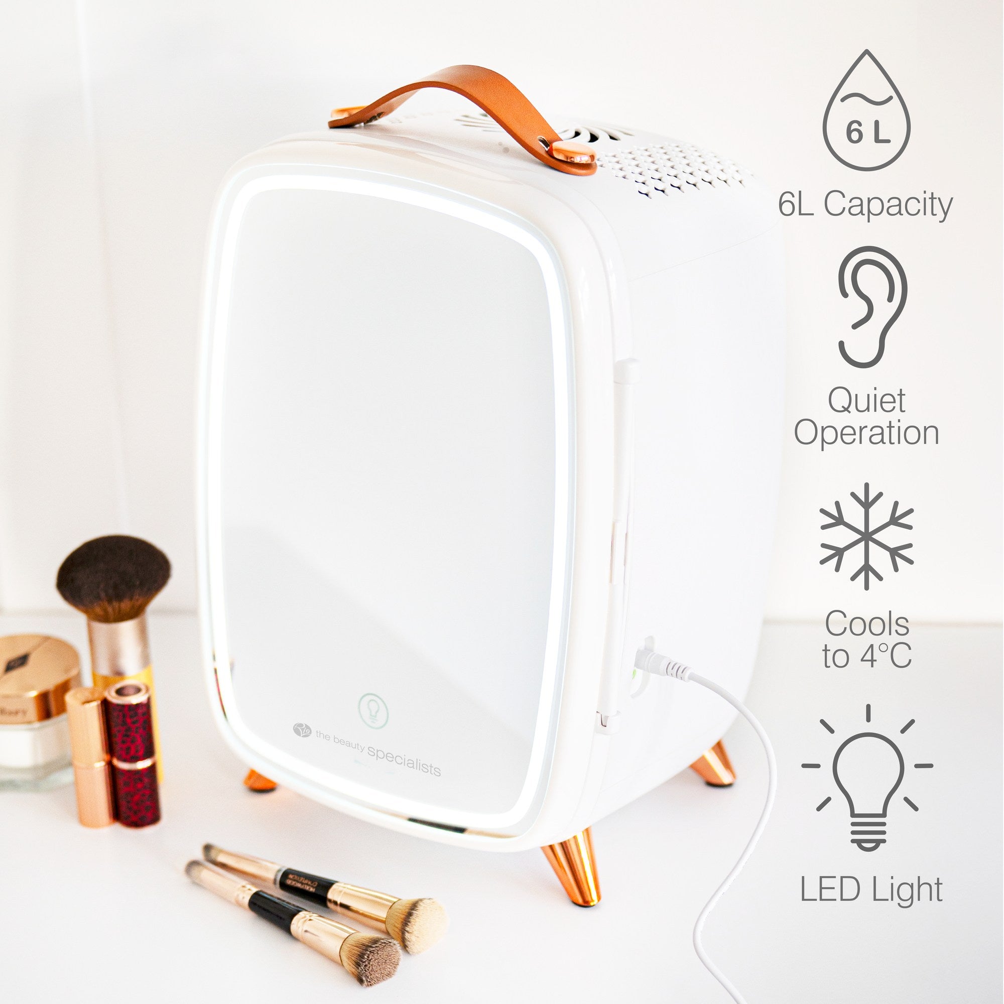 The Rio Beauty Skincare Fridge With Mirror, featuring a mirrored front and leather handle, sits on a vanity beside makeup brushes. It offers 6L capacity, quiet operation, chilling to 4°C, an LED light—ideal for cosmetics and creams.