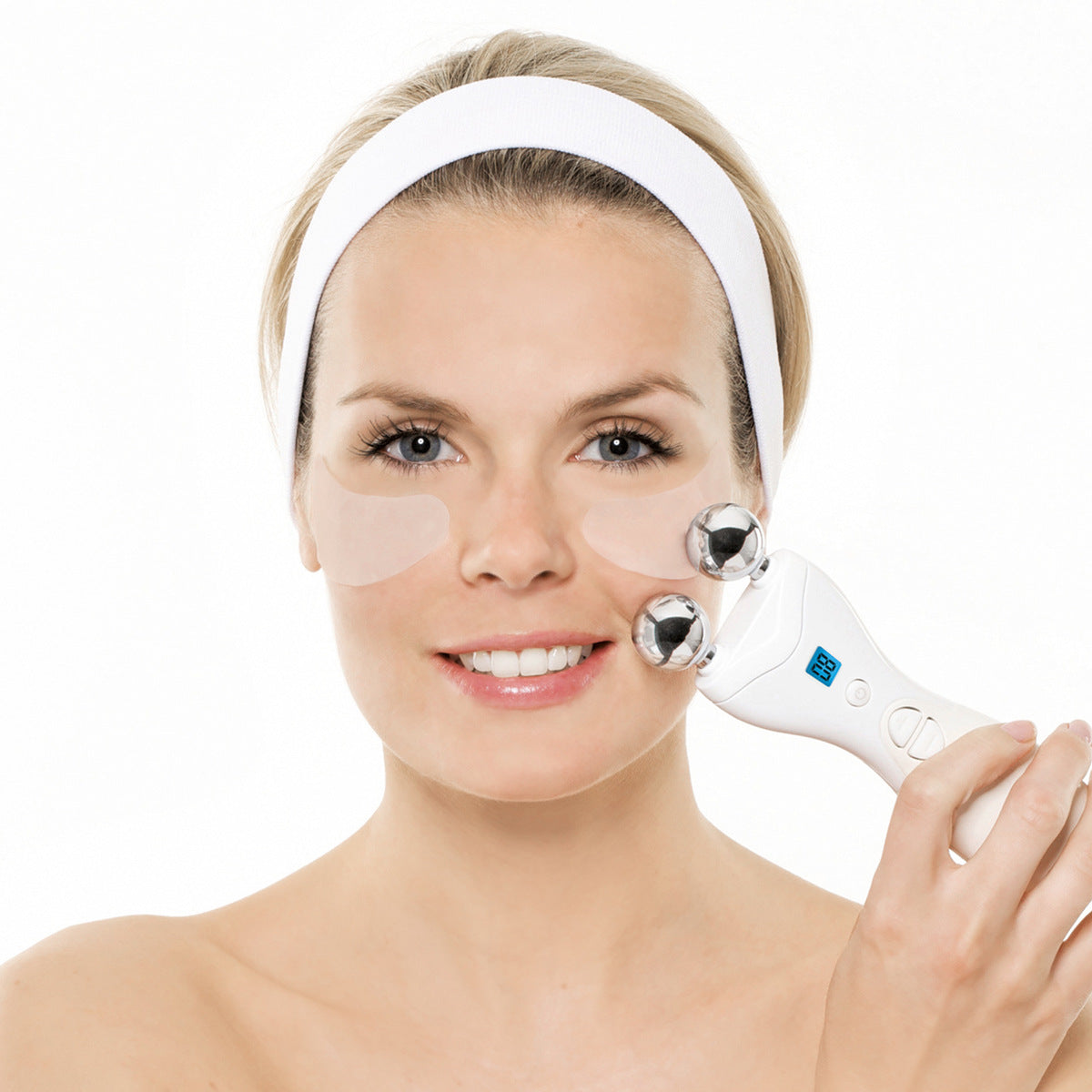 A woman with a white headband and under-eye patches smiles at the camera, using the Rio Lift Plus 60 Second Face Lift handheld massager with metal rollers on her cheek for instant face rejuvenation against a white background.