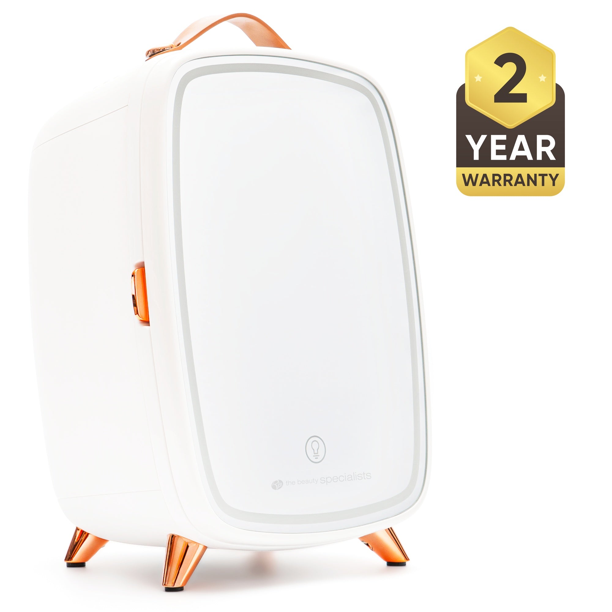 The Rio Beauty Skincare Fridge With Mirror is a sleek white mini fridge with copper accents, a leather handle, and four angled legs, ideal for chilling creams. A black and gold badge displays "2 Year Warranty" on the right side.