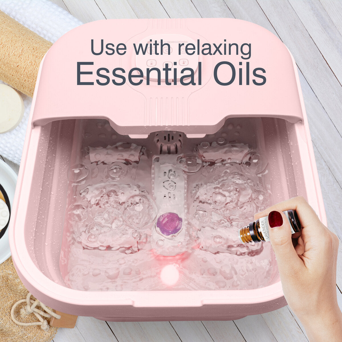A hand pours essential oil into the Rio Deluxe Foldaway Foot Spa Bath - Pink, filled with soothing water and bubbles. Text above reads: Use with relaxing Essential Oils.