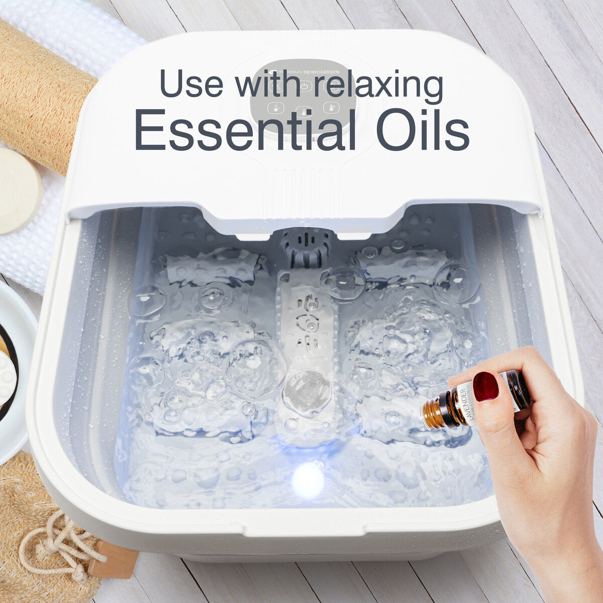 A person pours essential oil into the Rio Deluxe Foldaway Foot Spa Bath for a luxurious foot treatment; text above reads, Use with relaxing Essential Oils. Towels and soap can be seen nearby.