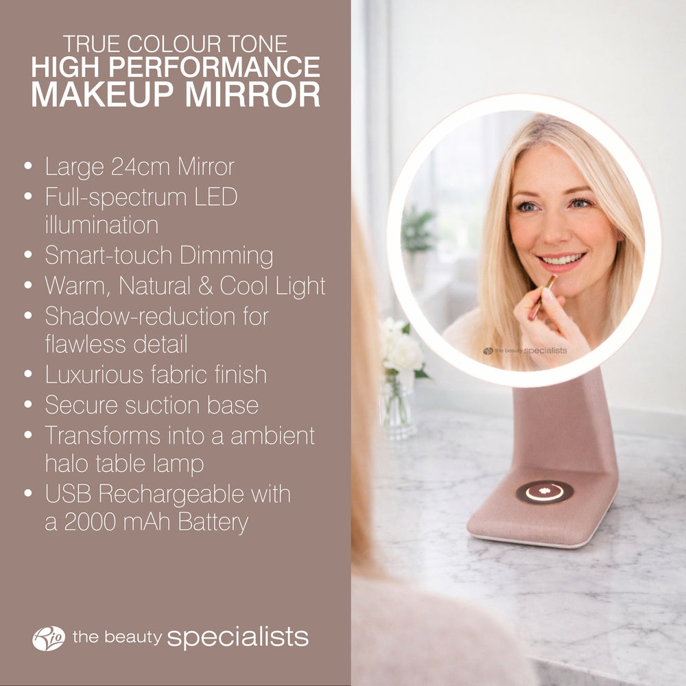 A woman applies lipstick, admiring herself in the Rio TrueColour High Performance Makeup Mirror. Warm LED light, dimming, fabric finish, and USB recharging are listed as features beside her as the round mirror softly glows on the table.