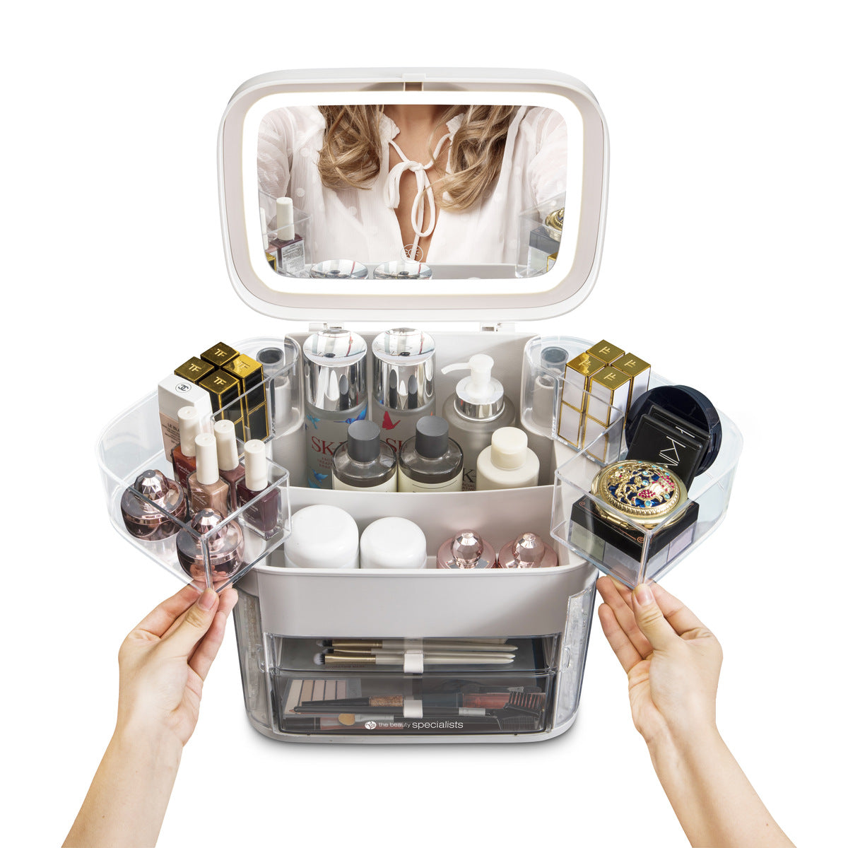 A person opens drawers of the Rio Ultimate Beauty Storage Box With Dimmable Mirror, revealing cosmetics, skincare, perfumes, and jewelry inside. The mirror reflects the person’s upper body in the background.