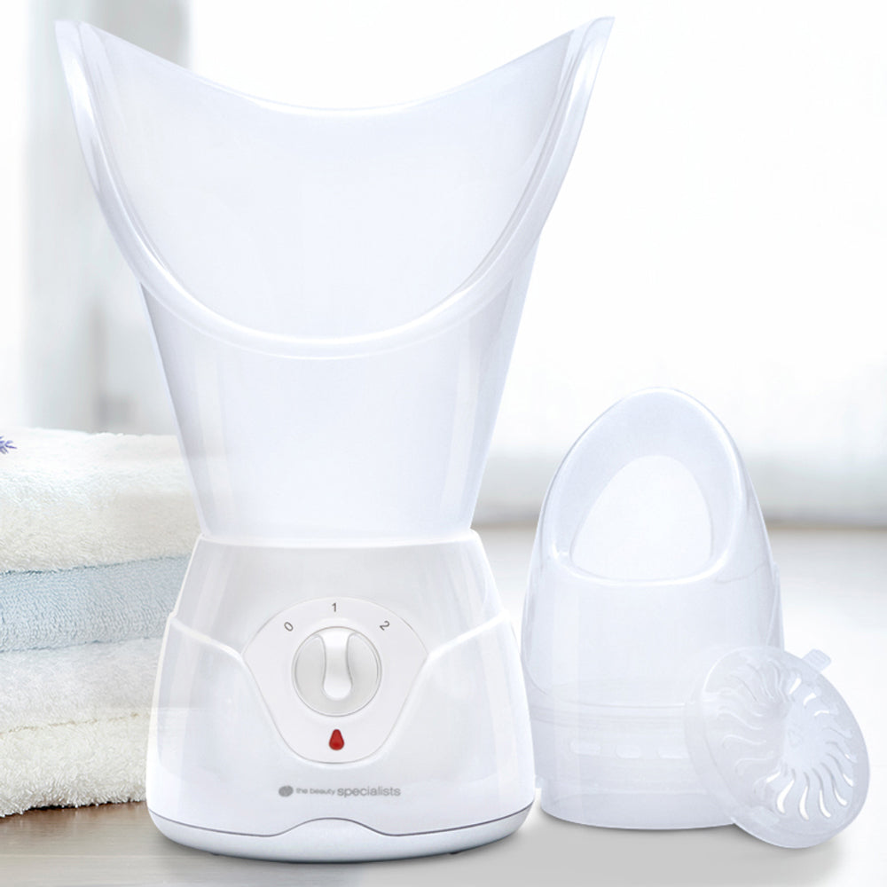 The Rio Facial Sauna Skincare with Steam Inhaler, featuring an adjustable dial, removable mask attachment, and compact cover, rests on a light surface beside folded towels.