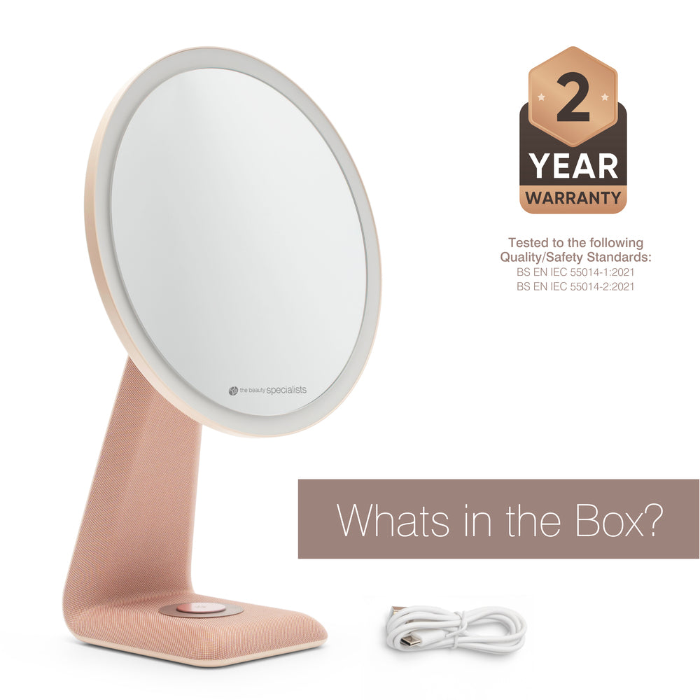The Rio TrueColour High Performance Makeup Mirror, a round rose gold design with high clarity and touch button on the stand, is shown beside a white charging cable. A 2 Year Warranty badge highlights its refined simplicity and quality.