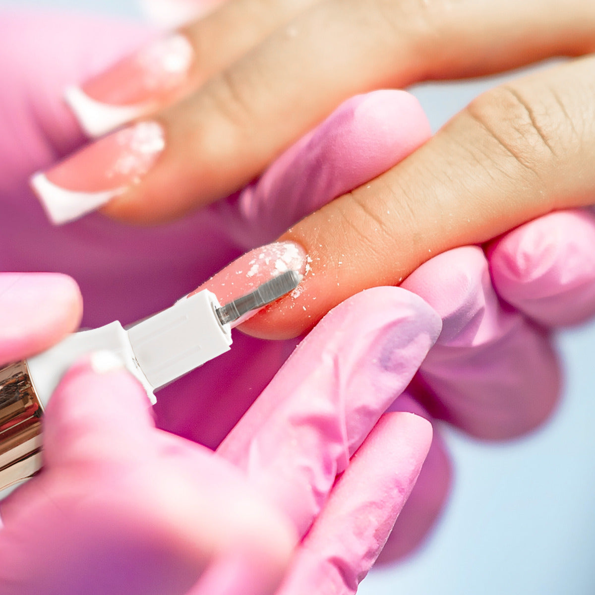 A close-up of gloved hands using the Rio Precision Pro Electric Nail File to expertly shape a pink and white French manicure, achieving professional nail care results.
