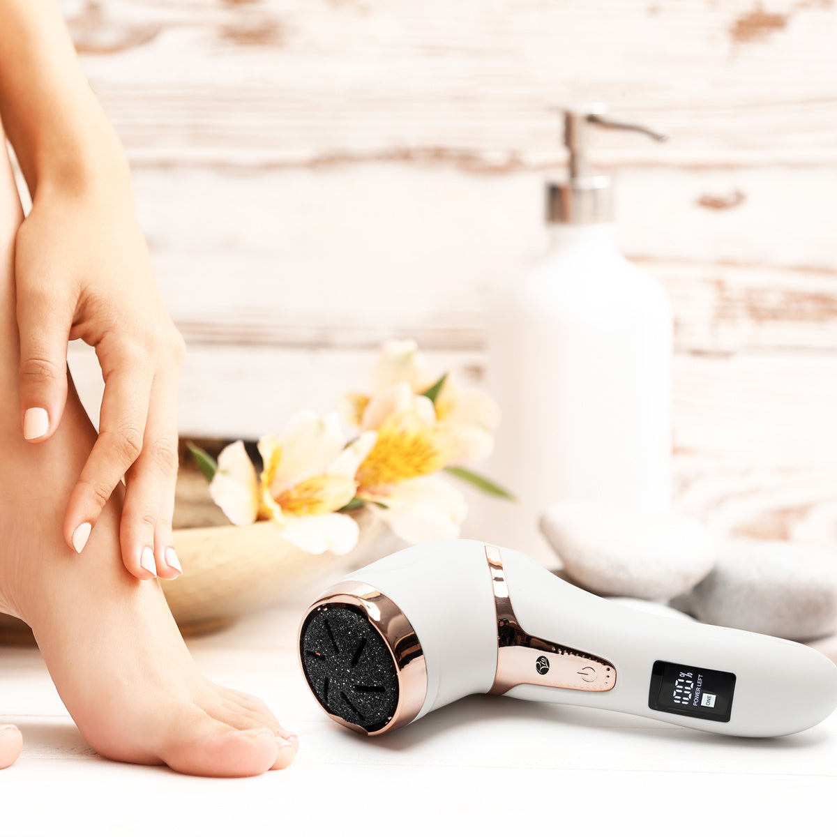 A person places their bare foot next to the Rio Go Smooth Electric Foot File Hard Skin Remover with Vacuum Action on a white surface, surrounded by spa-like elements—ideal for effective dry skin removal and silky smooth feet.