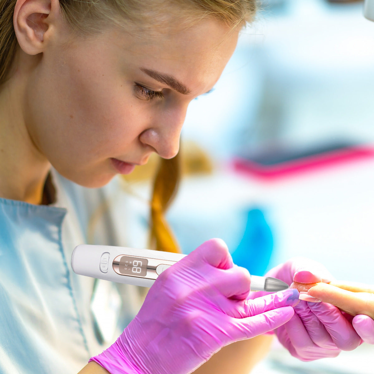 Wearing pink gloves, a woman expertly shapes a client’s nail using the Rio Precision Pro Electric Nail File, highlighting professional salon-quality nail care.