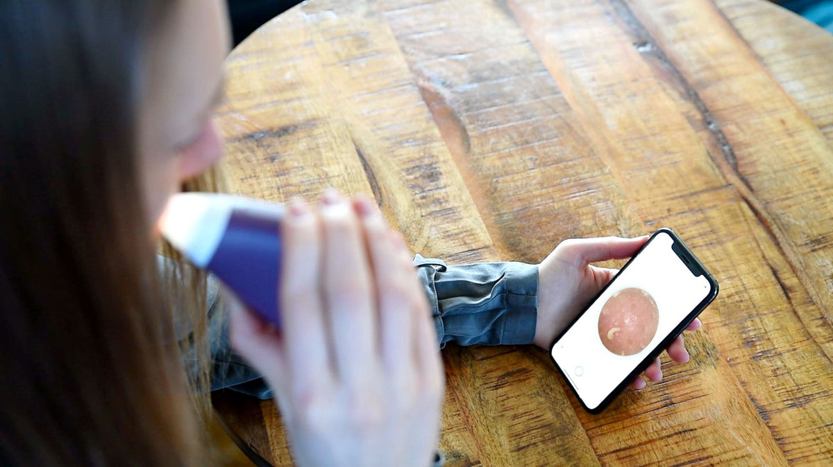 lady using pore perfector wireless on her face while watching live camera feed on smartphone 