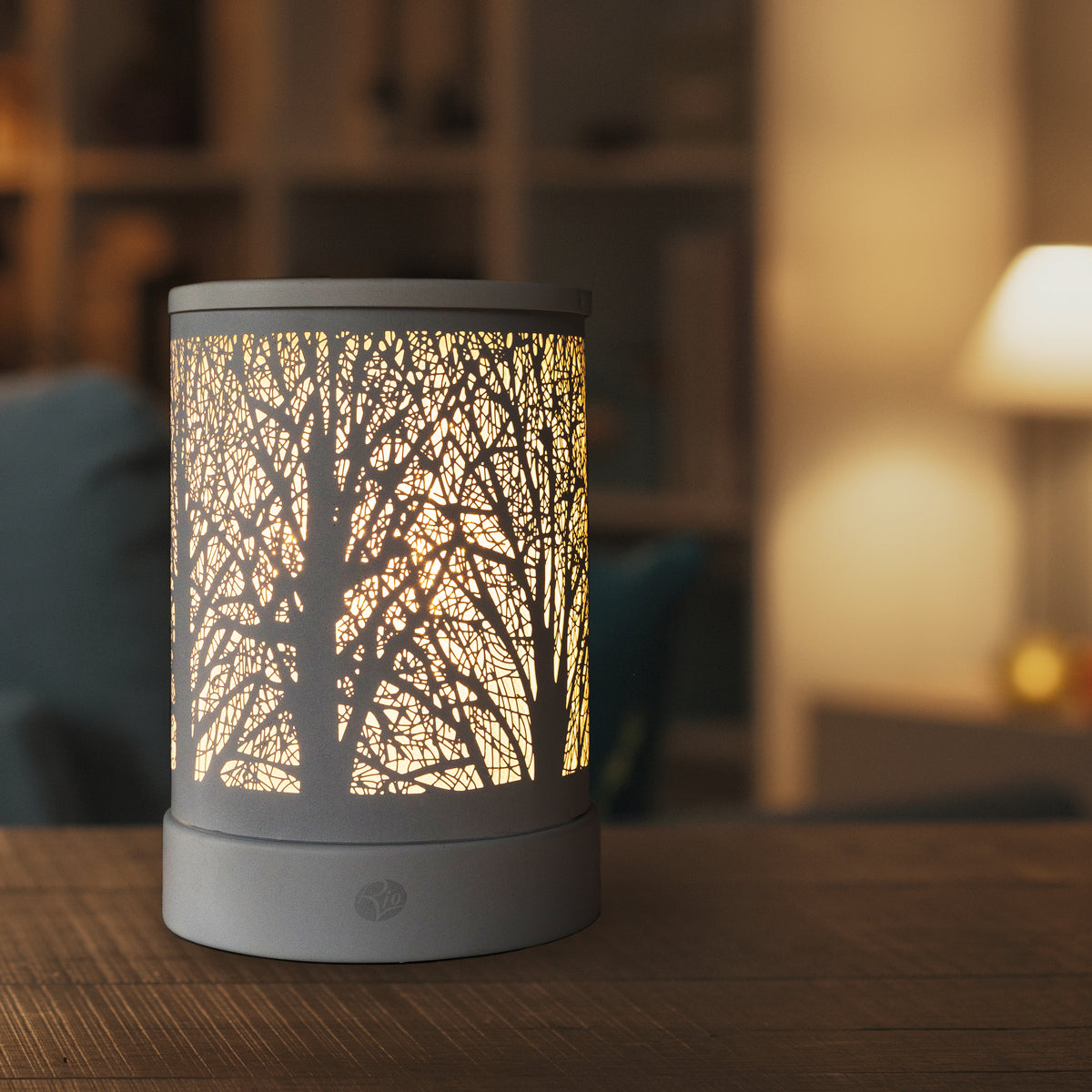 The Rio FORA Wax Melt Burner & Aroma Diffuser Lamp casts a warm, soft glow on your wooden table, enhancing your cozy living room with both style and soothing fragrance.