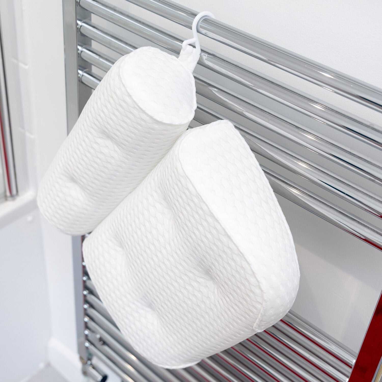 Two Rio Luxury Bath Spa Pillows in different shapes hang by their hooks on a chrome towel rail against a white bathroom wall, showcasing their quilted design, comfort, and style.