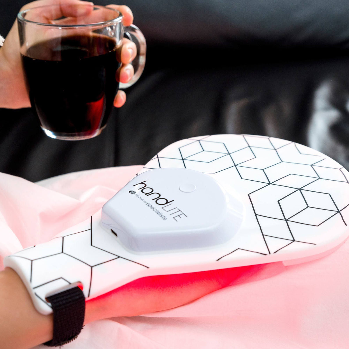 handLITE LED light treatment glove being worn whilst sat on sofa holding a glass of black coffee..